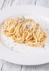 Creamy traditional carbonara served with grated parmesan on smooth white ceramic plate