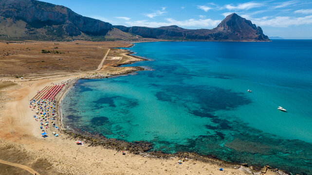 Aerial view of Macari Beach, located near San Vito Lo Capo in Sicily, Italy. In the background is a mountain called Monte Cofano, and the turquoise sea in the foreground.