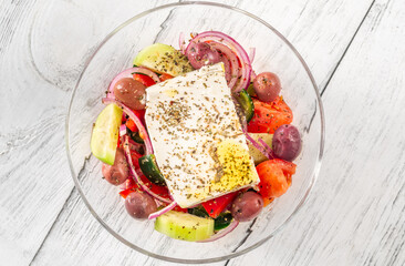 Fresh traditional Greek salad topped with thick feta slice served in glass bowl