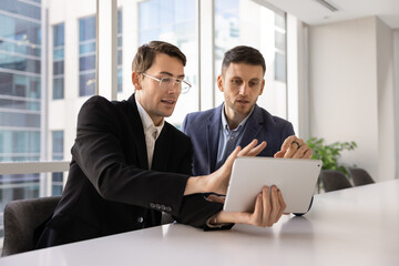 Two busy male professional colleagues working together with digital tablet
