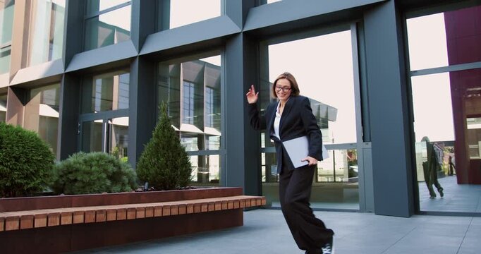Business outdoor and dancing with blond woman with laptop in hands emotionally gesturing while celebrating her success at work. Victory, lottery. Technology and business concept.
