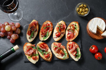 Delicious bruschettas with prosciutto and red wine served on black table, flat lay
