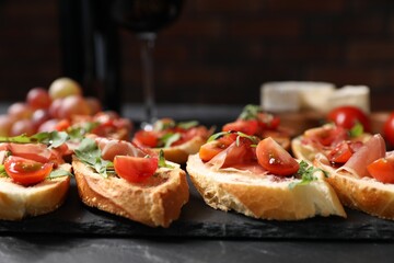 Delicious bruschettas with prosciutto served on black table, closeup