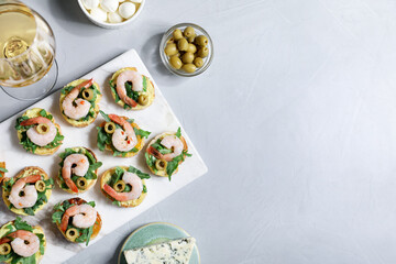 Delicious bruschettas with shrimps and wine on light table, flat lay. Space for text
