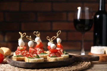 Delicious bruschettas with salami, mozzarella and tomatoes served with red wine on wooden table