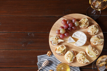 Delicious bruschettas served with camembert, grapes and wine on wooden table, flat lay. Space for text