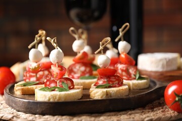 Delicious bruschettas with salami, mozzarella and tomatoes served with red wine on table, closeup