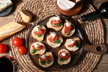 Delicious bruschettas with salami, mozzarella and tomatoes served with red wine on wooden table,...