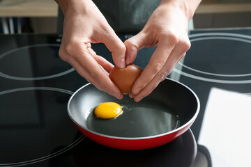 Woman cracking egg into frying pan in kitchen, closeup