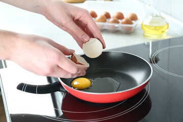 Woman cracking egg into frying pan in kitchen, closeup