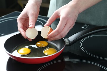 Woman cracking egg into frying pan in kitchen, closeup