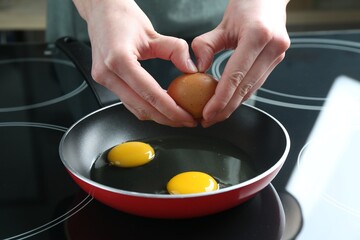 Woman cracking egg into frying pan in kitchen, closeup