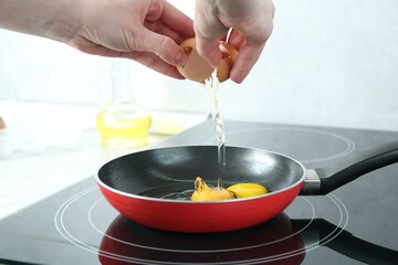Woman cracking egg into frying pan in kitchen, closeup