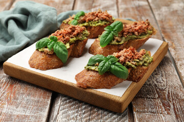 Delicious bruschettas with tuna, avocado and basil on wooden table, closeup