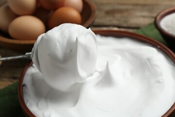 Whipped egg whites in bowl, whisk and ingredients on table, closeup