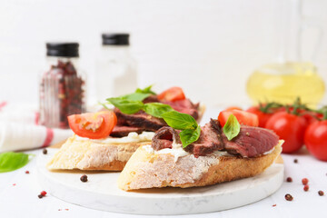 Delicious bruschettas with roast beef served on white table, closeup. Space for text
