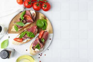 Delicious bruschettas with roast beef served on white tiled table, flat lay. Space for text