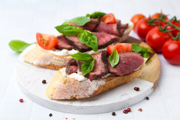 Delicious bruschettas with roast beef served on white tiled table, closeup