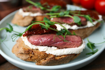Delicious bruschettas with roast beef served on wooden table, closeup