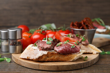 Delicious bruschettas with roast beef served on wooden table, closeup