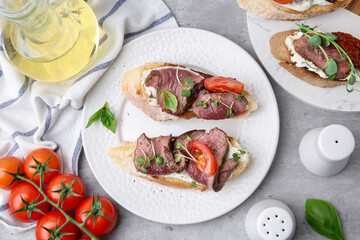 Delicious bruschettas with roast beef served on light table, flat lay