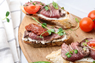 Delicious bruschettas with roast beef served on white table, closeup