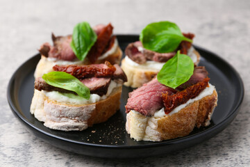 Bruschettas with roast beef, cream cheese, basil and sun-dried tomato on grey table, closeup
