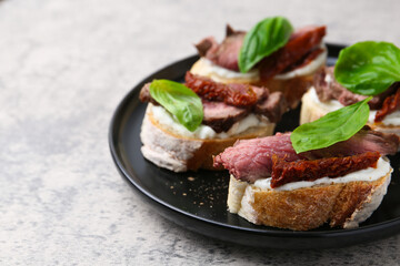 Bruschettas with roast beef, cream cheese, basil and sun-dried tomato on grey table, closeup. Space for text