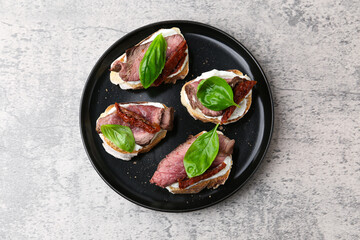Bruschettas with roast beef, cream cheese, basil and sun-dried tomato on grey table, top view