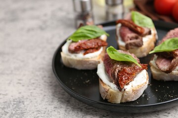 Bruschettas with roast beef, cream cheese, basil and sun-dried tomato on grey table, closeup. Space for text