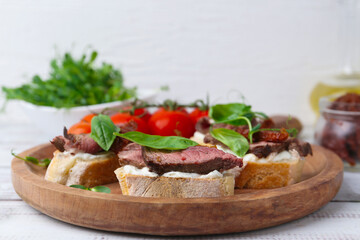 Bruschettas with roast beef served on white wooden table, closeup