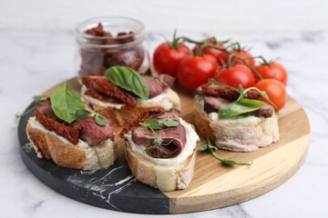 Bruschettas with roast beef, cream cheese, basil, sun-dried tomatoes and fresh vegetables on white marble table, closeup
