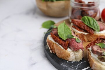 Bruschettas with roast beef, cream cheese, basil and sun-dried tomatoes on white marble table, closeup. Space for text