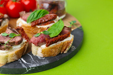 Bruschettas with roast beef, cream cheese, basil, sun-dried tomatoes and fresh vegetables on green background, closeup. Space for text