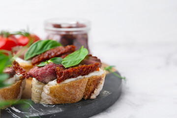 Bruschettas with roast beef, cream cheese, basil, sun-dried tomatoes and fresh vegetables on white marble table, closeup. Space for text