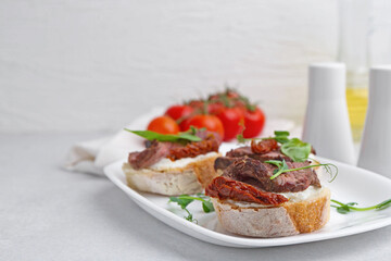 Bruschettas with roast beef, cream cheese, basil, sun-dried tomatoes and fresh vegetables on light grey table, closeup. Space for text