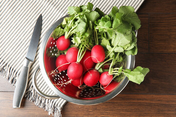 Fresh ripe radishes in colander and knife on wooden table, top view