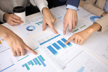 Hands of analysts pointing at paper diagrams on meeting table
