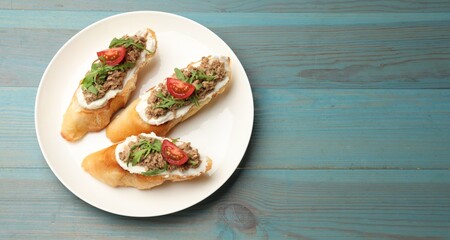 Delicious bruschettas with tuna, cream cheese and tomatoes on light blue wooden table, top view. Space for text