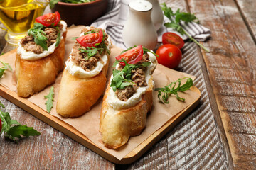 Delicious bruschettas with tuna, tomatoes and arugula on wooden table, closeup