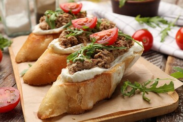 Delicious bruschettas with tuna, cream cheese and tomatoes on wooden table, closeup
