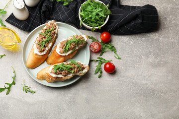 Delicious bruschettas with tuna, tomatoes, oil and arugula on grey table, flat lay. Space for text