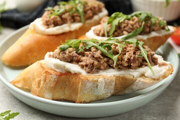 Delicious bruschettas with tuna, cream cheese and arugula on grey table, closeup