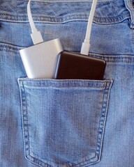 External battery and smartphone charger in a jeans pocket. Phone and portable charger in a denim pocket.