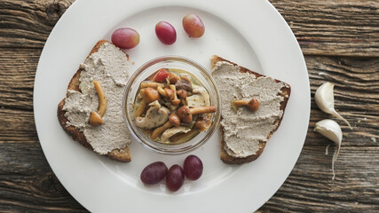Delicious mushrooms served on toasted bread with fresh grapes and garlic on rustic wooden table