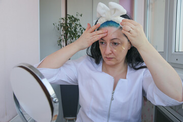An adult mature woman takes care of her facial skin while sitting in front of a mirror.