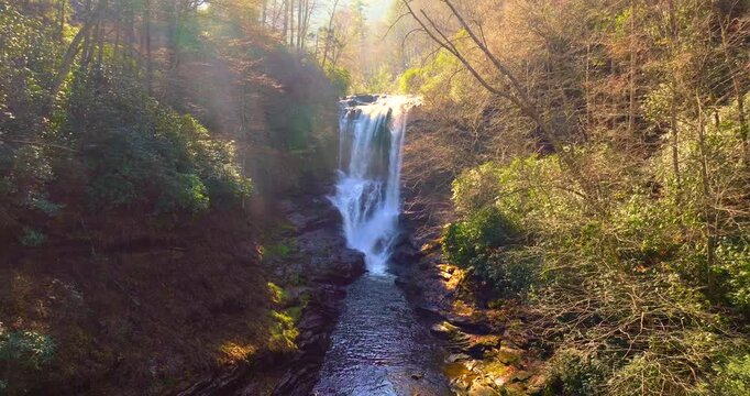 Autumn landscape at Dry Falls, North Carolina. Clear water tumbles from rocky boulders framed by orange and yellow forest trees