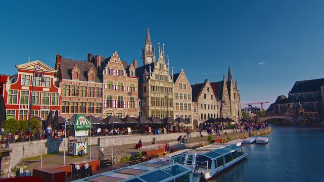 Ghent, Belgium - 15.08.2025: View of an old waterfront with traditional architecture and people strolling on a sunny summer day in the Flemish Region of Belgium. Timelapse