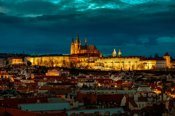 Illuminated Saint Vitus Cathedral, against a dramatic twilight sky overlooking the red rooftops of Mala Strana in Prague, Czechia.