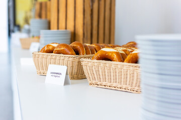 Close-up of a buffet with fresh pretzels in the foreground. The pretzels are placed in a wicker basket, with stacked plates visible in the background.